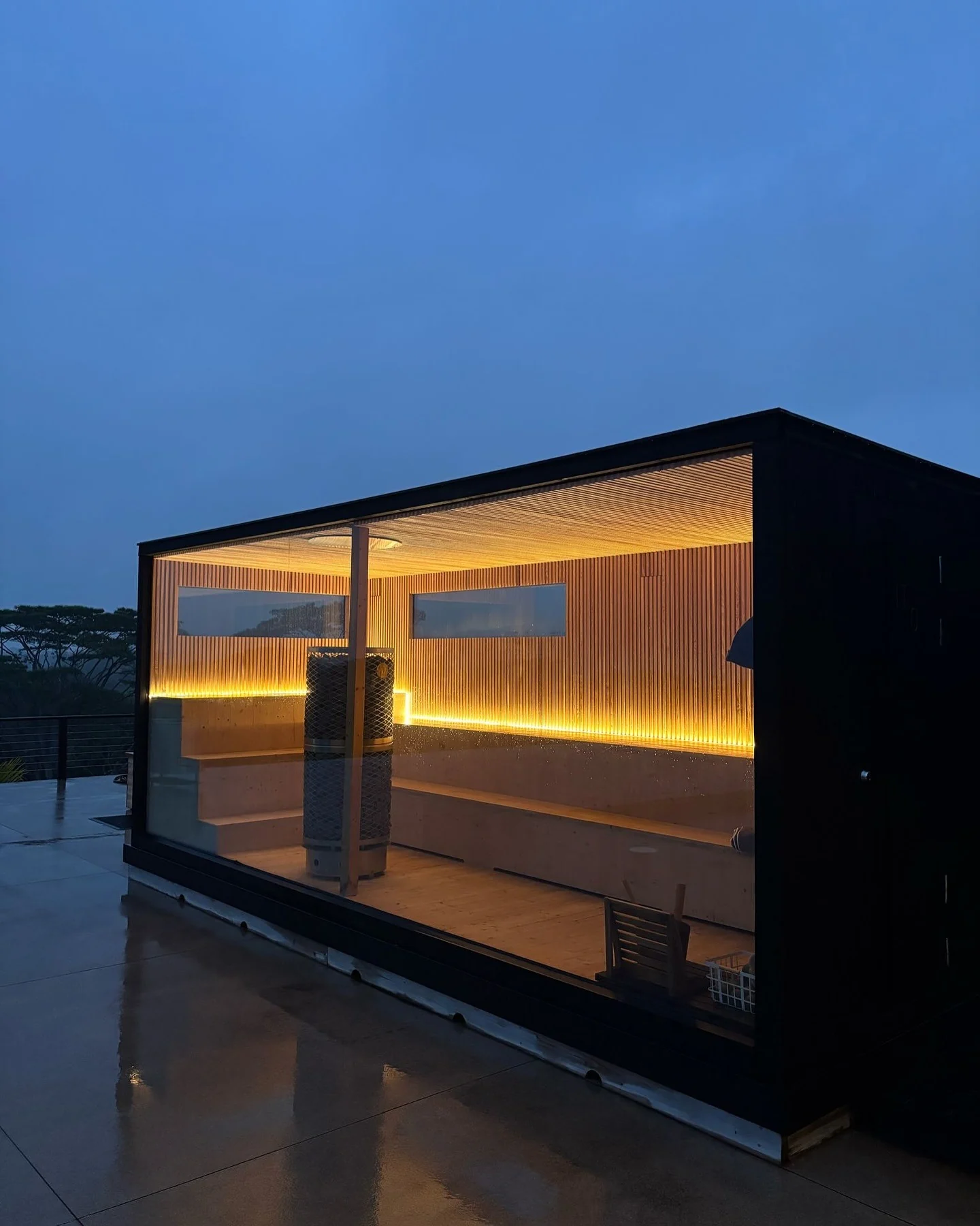 Modern glass-front outdoor sauna at dusk