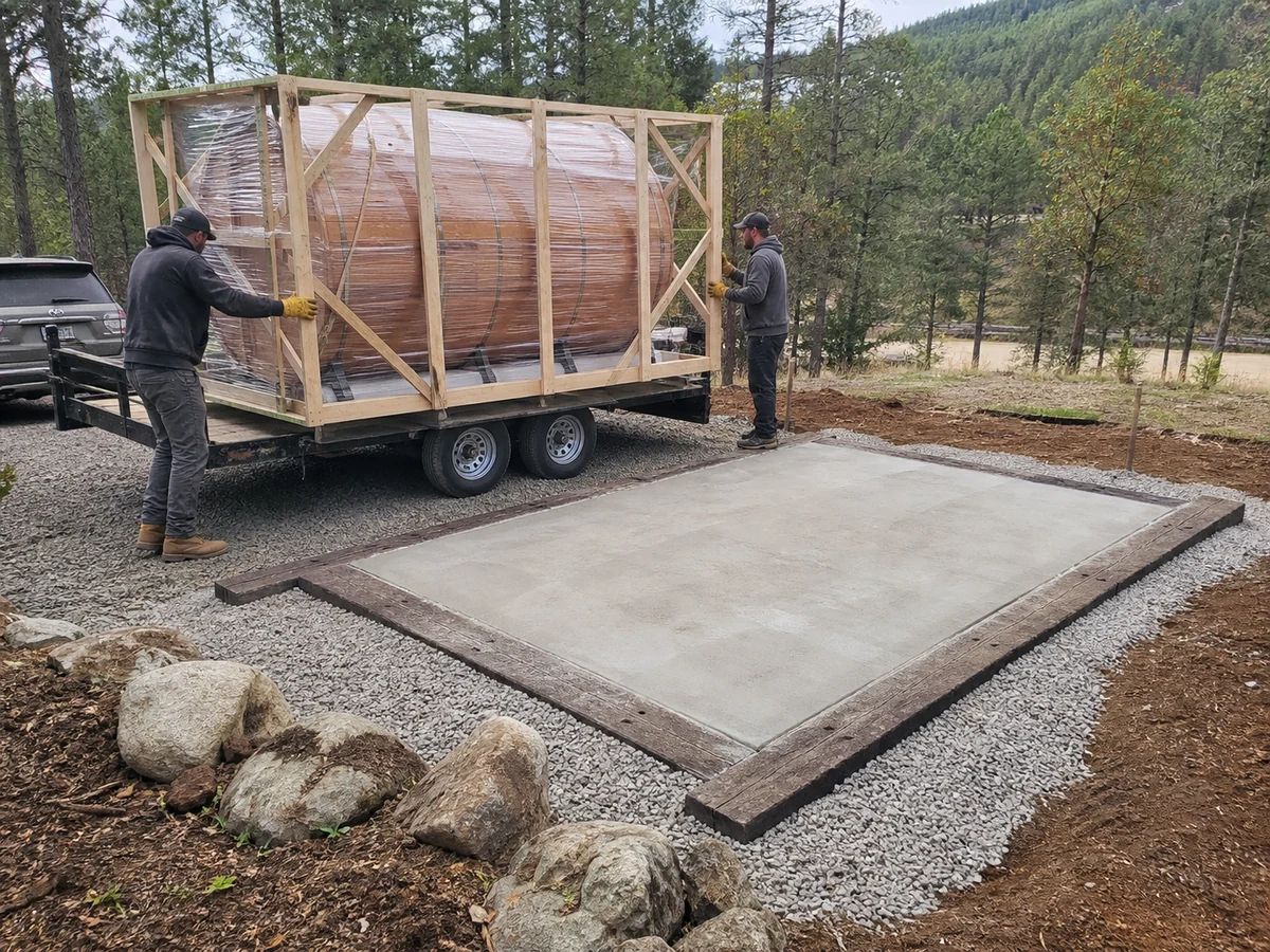 Barrel sauna delivery approaching a prepared level foundation with drainage and service access