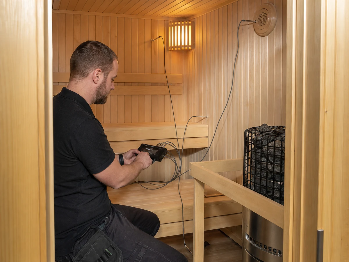 Commissioning technician recording sauna temperatures at upper bench foot zone controller and ventilation points
